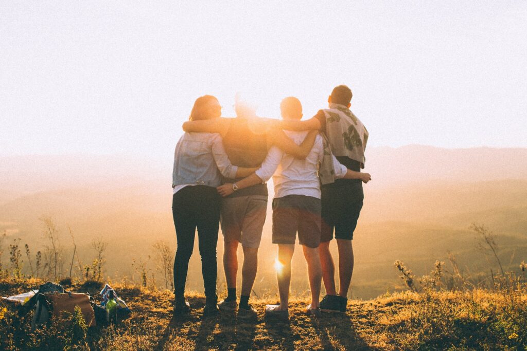 cuatro personas se rodean los hombros con las manos mientras miran la puesta de sol