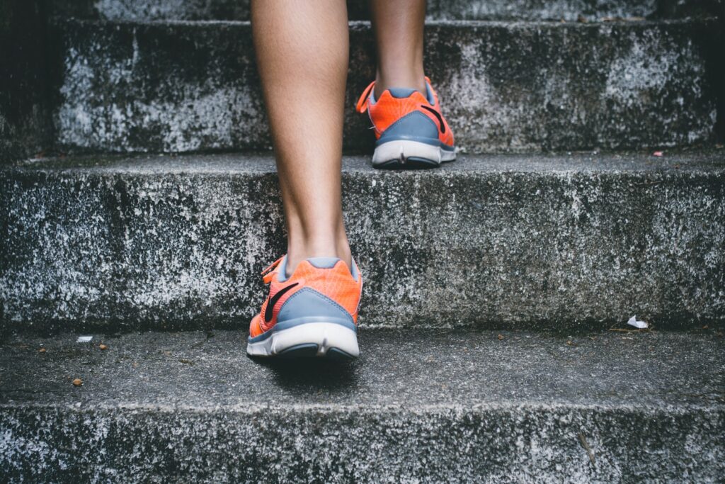 pessoa com sapatos Nike cor-de-laranja e cinzentos a andar em escadas de betão cinzento